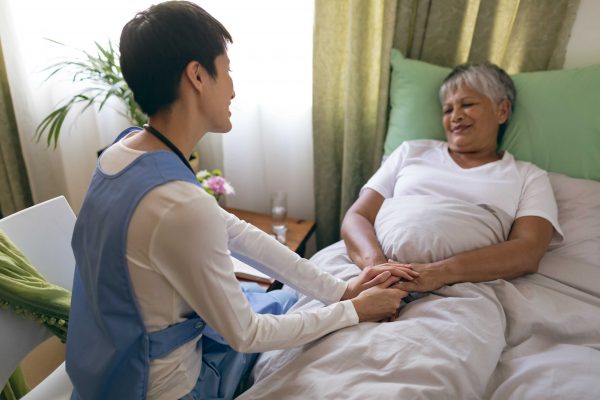 Front view of Asian female nurse taking care of senior mixed race  female patient at retirement home. Senior female is lying in bed.